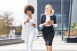 © GER/Westend61 - Smiling businesswomen walking with smart phone and digital tablet on footpath