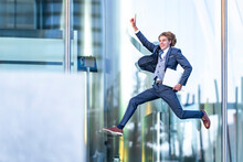 Cheerful Male Entrepreneur With Laptop Gesturing While Jumping Against Glass Office Building