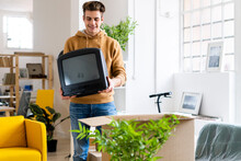 Young Man Carrying Television Set While Moving Into New Home