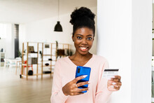 Young Woman With Credit Card Smiling While Shopping Through Mobile Phone Standing At Home