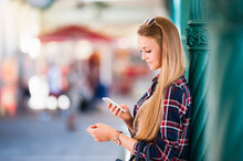 Young Woman Leaning Against Column Looking At Smartphone