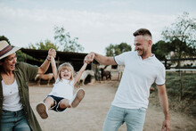 Playful Parents Holding Daughter's Hands And Swinging Her While Standing On Land