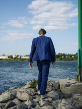 Businessman Wearing Suit Walking On Rocks At Rhine Riverbank Against Sky
