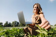 © KNSY/Westend61 - Young woman with laptop caring for plants in a vegetable patch