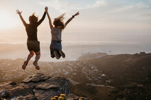 South Africa, Cape Town, Kloof Nek, Two Women Jumping On Rock At Sunset