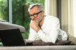 © steve brookland/Westend61 - Smiling senior man with grey hair in modern design living room working on laptop