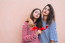 Sisters Holding Hibiscus Flowers While Standing Against Wall