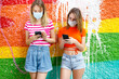 © Ignacio Ferr√°ndiz Roig/Westend61 - Fashionable female friends in shorts using smart phones against graffiti wall during pandemic