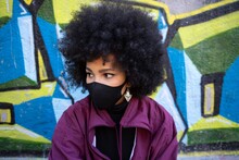Young Woman Wearing Protective Face Mask Looking Away Against Graffiti Wall