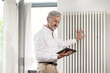© steve brookland/Westend61 - Senior man with grey hair in modern design living room holding tablet checking his smarthome heating