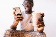 © Oscar Carrascosa/Westend61 - Smiling young man using smart phone while sitting with disposable coffee cup against white background