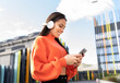 © Jose Carlos Ichiro/Westend61 - Portrait of beautiful brunette standing outdoors and smiling while listening to music on headphones