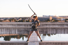 Young Female Sportsperson Practicing Sword On Structure Against Clear Sky At Sunset