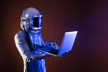 Male astronaut in space suit using laptop while standing by colored background