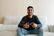 © Ezequiel Gim√©nez/Westend61 - Smiling young man sitting on sofa while playing video game at home