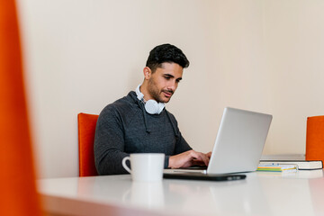 Young man with headphone using laptop while sitting at table in living room