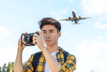 Portrait Of Young Tourist With Camera With Airplane Above Him