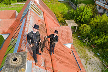 Portrait Of Two Smiling Chimney Sweeps Standing On House Roof