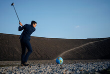 Mature Businessman Playing Golf With A Globe On A Disused Mine Tip