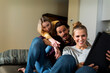 © VALENTINA BARRETO PHOTOGRAPHY/Westend61 - Friends sitting on couch in livingroom, having fun, using laptop