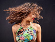 © Veam/Westend61 - Smiling young woman tossing her curly hair in front of dark background