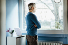 Pensive Man Standing In Living Room Looking Out Of Window