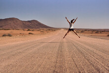 Woman jumping in the middle of a dirt road, Damaraland, Namibia
