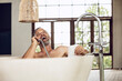 © Maya Claussen/Westend61 - Laughing man in bathtub using shower head as telephone receiver