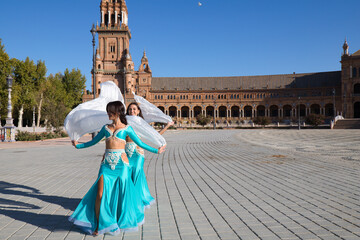 Two young and beautiful belly dancers dancing in a square. They are dressed in light blue with white veils in their hands. World folklore concept from Africa and Asia.