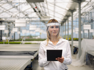 Businesswoman wearing face shield with digital tablet working in plant nursery