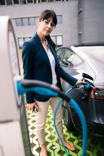 Female Entrepreneur Plugging Charger To Electric Car At Station