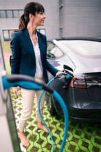 Mature Businesswoman Looking Away While Plugging Charger To Electric Car
