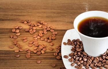 Coffee beans with a cup of filter coffee on brown wooden background.	