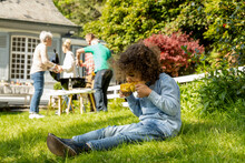 Boy Eating A Corn Cob On A Family Barbecue In Garden
