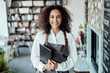 © Joseffson/Westend61 - Smiling woman wearing apron holding book while standing at cafe