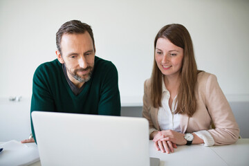 Businessman and employee using laptop at desk in office