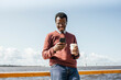 © Vasily Pindyurin/Westend61 - Young man standing at the sea, holding coffee, using smartphone