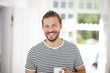 © MiJo/Westend61 - Portrait of smiling young man holding cup of coffee at home