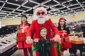 Wall Mural - Portrait of attractive funky cheerful group friends elfs buying digital goods driving scooter having fun at store market indoors