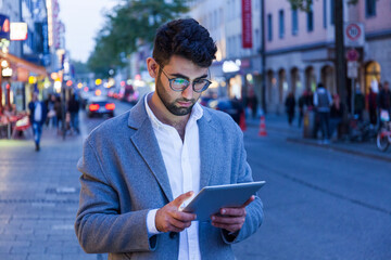 Germany, Munich, young businessman using digital tablet in the city at dusk
