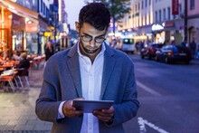 Germany, Munich, Young Businessman Using Digital Tablet In The City At Dusk