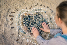 Little Girl Making A Heart From Seashells On The Beach