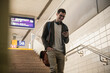 © Uwe Umst√§tter/Westend61 - Smiling young man with cell phone walking down stairs at the station
