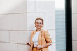 © Katharina Mikhrin/Westend61 - Smiling female entrepreneur with smart phone while standing against wall