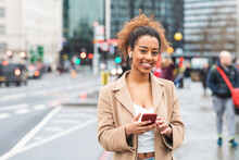 Smiling Young Woman With Cell Phone And Earbuds In The City, London, UK