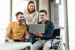 © UWE_UMSTAETTER/Westend61 - Young businessman in wheelchair showing laptop to colleagues in office