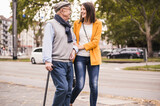 Fototapeta Las - Adult granddaughter assisting her grandfather strolling with walking stick