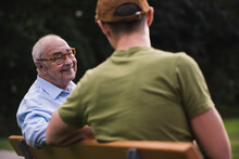 Portrait Of Smiling Senior Man Relaxing Together With His Grandson On A Park Bench