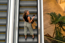 Woman With Shopping Bag Standing On Escalator At Mall