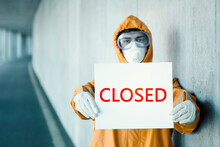 Portrait Of Man Wearing Protective Clothing Holding A 'closed' Sign